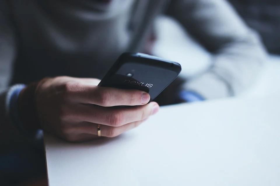 A person’s hand holding a black smartphone over a white table.