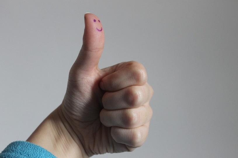 A person making a thumbs-up gesture, with their thumb having a smiley face drawn on it.