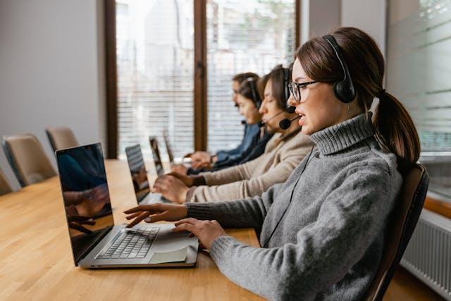 Women on laptops, with headsets, attending calls at one table.