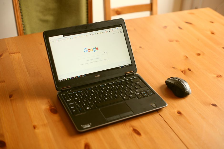 Laptop and mouse on a wooden desk showing a browser homepage