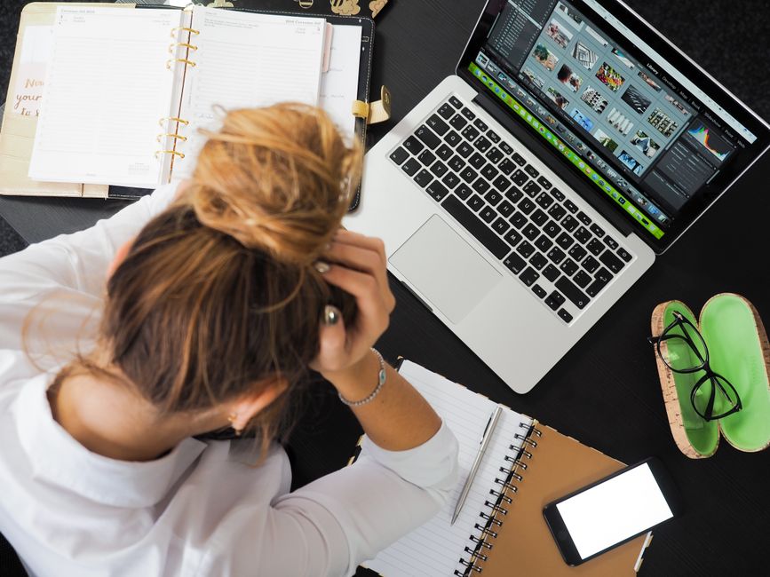 Person working at a desk with a laptop, head in hands