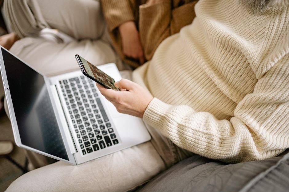 Person holding a smartphone while using a laptop at home