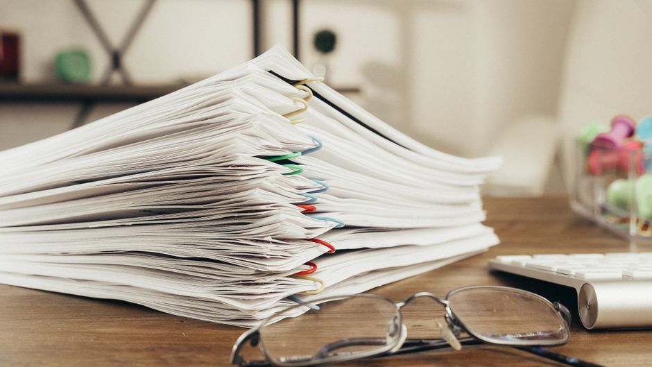 A stack of paper documents held together with clips on an office desk