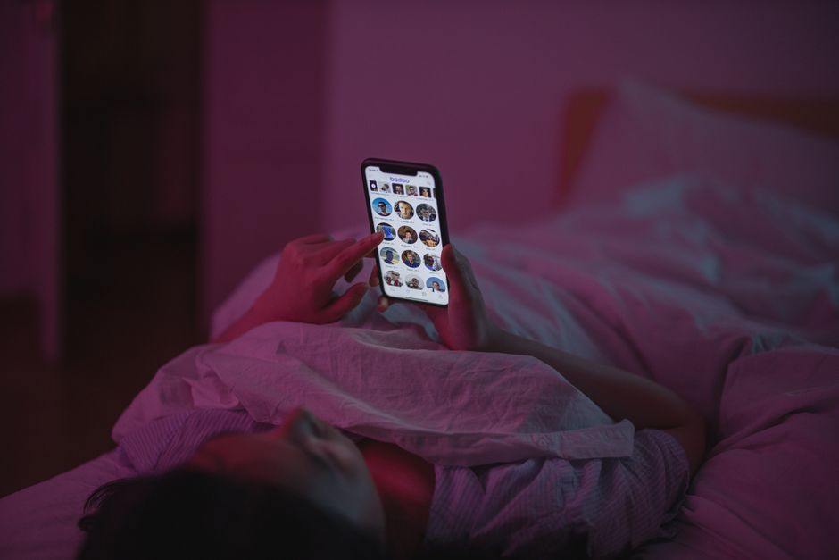 Woman using her smartphone while lying in bed at night