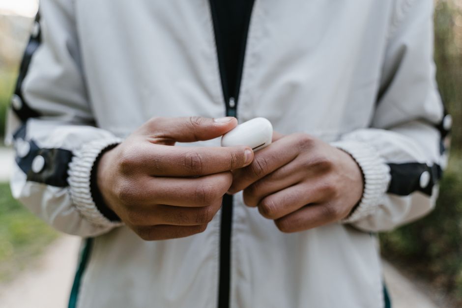Person holding an open case of wireless earbuds outdoors