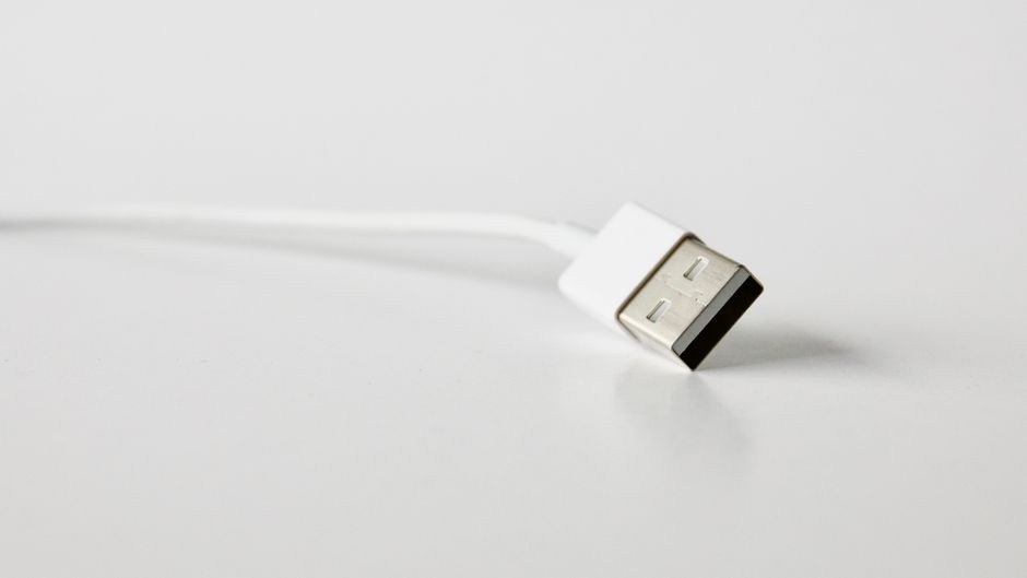 Close-up of a white USB charging cable held between fingers