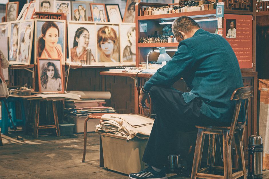 An artist intensely focused, surrounded by portraits in a Beijing studio.