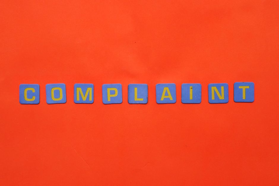 Blue letter tiles spelling 'COMPLAINT' on a vibrant red surface.